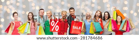 consumerism, people and discount concept - group of happy people with percentage and sale sign on shopping bags over holidays lights background