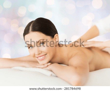 people, beauty, spa, holidays and body care concept - happy beautiful woman having back massage over blue lights background