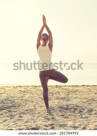 fitness, sport, people and lifestyle concept - woman making yoga exercises on sand outdoors from back