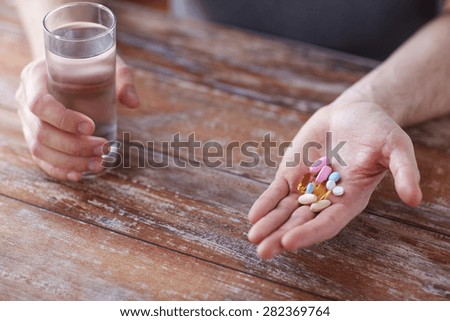 healthy lifestyle, medicine, nutritional supplements and people concept - close up of male hands holding pills with cod liver oil capsules and water glass