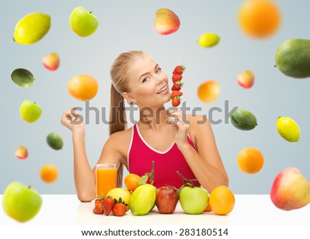 healthy eating, diet, detox, organic food and people concept - happy young woman with juice and fruits eating strawberries over gray background