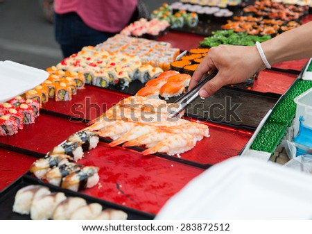 cooking, asian kitchen, sale and food concept - close up of hand with tongs taking sushi at street market
