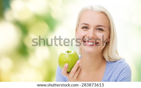 healthy eating, organic food, fruits, diet and people concept - happy woman eating green apple over green natural background