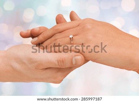jewelry, couple, love and wedding concept - close up of man and woman hands with engagement ring over blue holidays lights background