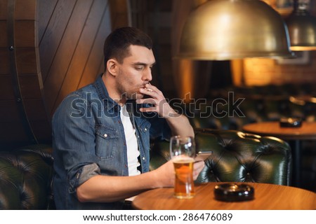people and bad habits concept - man drinking beer and smoking cigarette at bar or pub