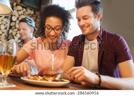 people, leisure, friendship, party and communication concept - group of happy smiling friends eating burger together at bar or pub