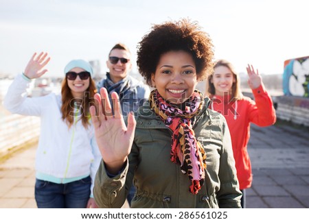 people, friendship and international concept - happy african american young woman or teenage girl in front of her friends waving hands on city street