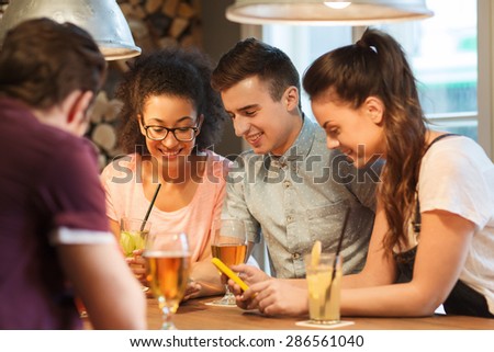 people, leisure, friendship, technology and communication concept - group of happy smiling friends with smartphones and drinks at bar or pub