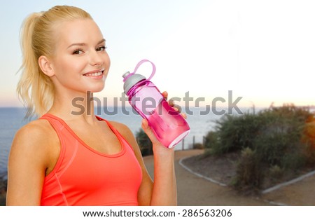 people, sport, fitness, jogging and recreation concept - happy woman drinking water from bottle over beach sunset background