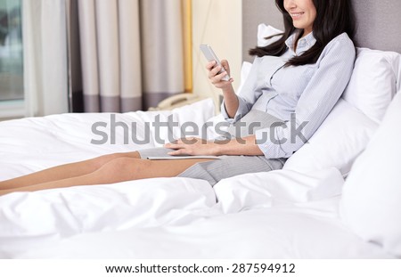 business trip, people and technology concept - smiling businesswoman with smartphone typing in bed at hotel