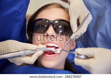 people, medicine, stomatology and health care concept - female dentists with mirror, drill and probe treating patient girl teeth at dental clinic office