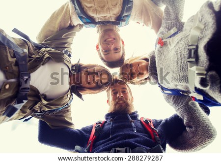 adventure, travel, tourism, hike and people concept - group of smiling friends with backpacks standing in circle and holding to each other outdoors
