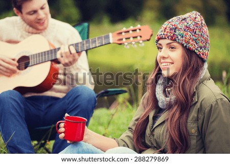 adventure, travel, tourism and people concept - smiling couple with guitar in camping