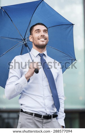 business, bad weather and people and concept - young smiling businessman with umbrella outdoors