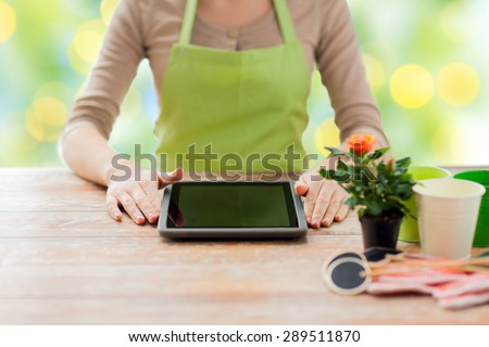 people, gardening, flowers and profession concept - close up of woman or gardener with tablet pc computer sitting at wooden table over green lights background