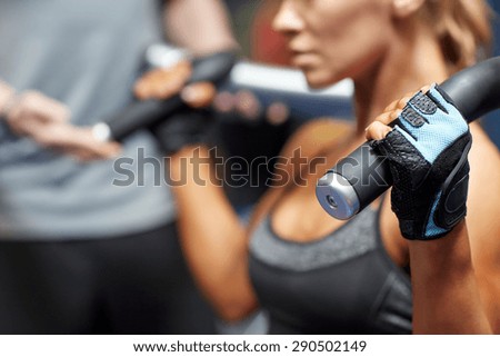 sport, fitness, bodybuilding, teamwork and people concept - young woman and personal trainer flexing muscles on gym machine