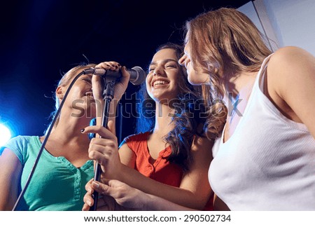 party, holidays, celebration, nightlife and people concept - happy young women singing karaoke in night club
