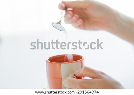 food, junk-food, drinks and unhealthy eating concept - close up of woman hands with spoon adding sugar to tea cup