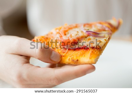 people, fast food, italian kitchen and eating concept - close up of hand holding pizza slice