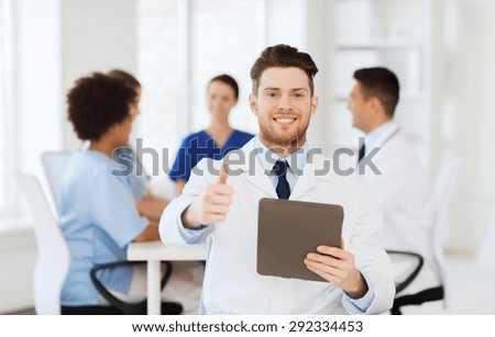 clinic, profession, people and medicine concept - happy male doctor with tablet pc computer over group of medics meeting at hospital showing thumbs up gesture