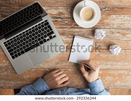 business, education, people and technology concept - close up of male hands with laptop and coffee cup taking notes to notebook by pen