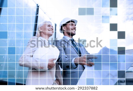 business, partnership, architecture and people concept - smiling businessman and businesswoman with blueprint and helmets over city street and blue grid background