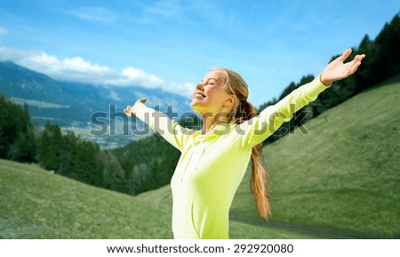 fitness, sport, people and emotions concept - happy woman in sportswear enjoying sun and freedom over mountains, green fields and blue sky background