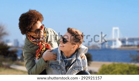friendship, travel, tourism and people concept - happy international teenage couple in shades having fun over rainbow bridge at tokyo in japan background