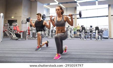 sport, bodybuilding, lifestyle and people concept - young man and woman with barbell flexing muscles and making shoulder press lunge in gym