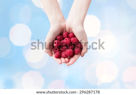 healthy eating, dieting, vegetarian food and people concept - close up of woman hands holding ripe raspberries over blue lights background