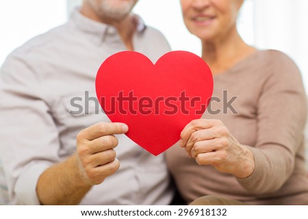 family, holidays, valentines day, age and people concept - close up of happy senior couple holding big red paper heart shape cutout at home