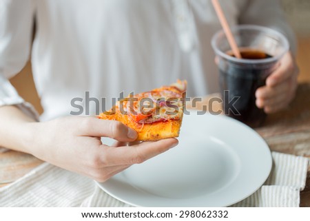 fast food, people and unhealthy eating concept - close up of woman hands with pizza and drink sitting at table