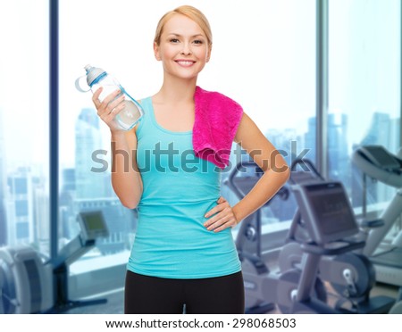 people, sport, fitness and recreation concept - happy woman with bottle of water and towel over gym machines background