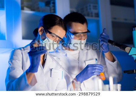 science, chemistry, biology, medicine and people concept - close up of young scientists with pipette and flasks making test or research in clinical laboratory
