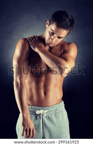 pain relief, sport, bodybuilding, health and people concept - young man standing over black background