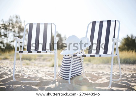 furniture and summer holidays concept - two beach lounges with beach bag and white hat on the beach