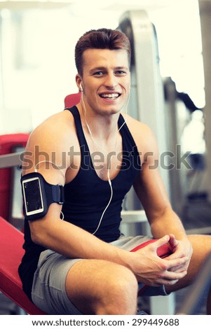 sport, bodybuilding, lifestyle, technology and people concept - smiling young man with smartphone and earphones in gym