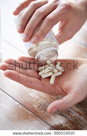 sport, healthy lifestyle, medicine, nutritional supplements and people concept - close up of man pouring pills from jar to hand