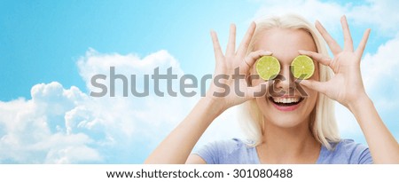 healthy eating, organic food, fruit diet, comic and people concept - happy woman having fun and covering her eyes with lime slices over blue sky and clouds background