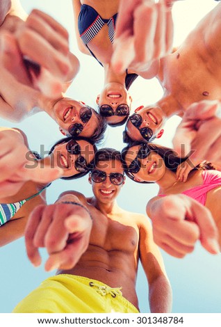 friendship, summer vacation, gesture and people concept - group of smiling friends wearing swimwear and pointing finger on you standing in circle over blue sky