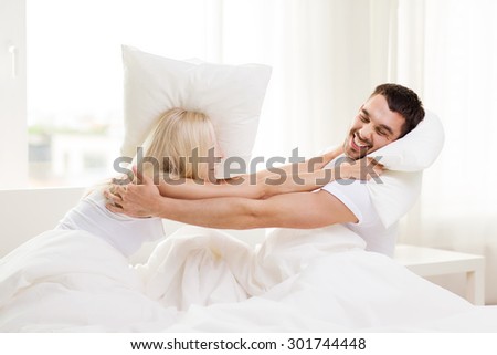 people, family, bedtime and fun concept - happy couple having pillow fight in bed at home