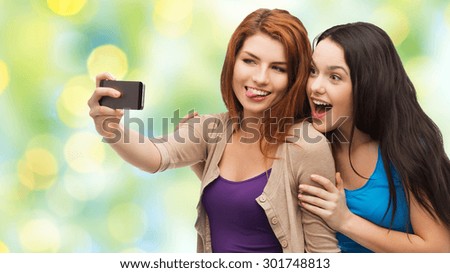 technology, friendship and people concept - two smiling teenage girls or young women taking selfie with smartphone over green lights background