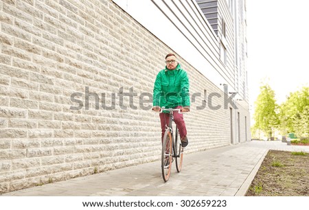 people, style, leisure and lifestyle - young hipster man riding fixed gear bike on city street over building brick wall background