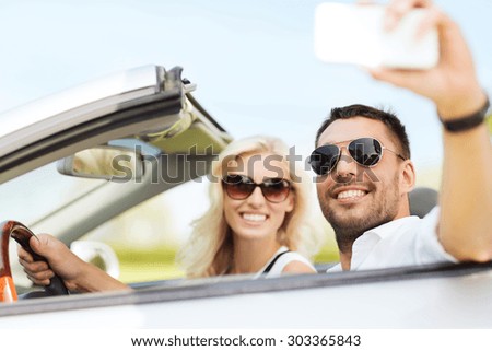 road trip, leisure, couple, technology and people concept - happy man and woman driving in cabriolet car and taking selfie with smartphone