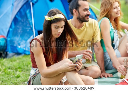 travel, tourism, hike, technology and people concept - happy young woman with smartphone and friends at camping