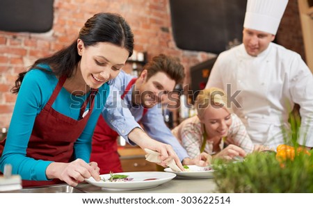 cooking class, culinary, food and people concept - happy couple and male chef cook cooking and decorating plates in kitchen