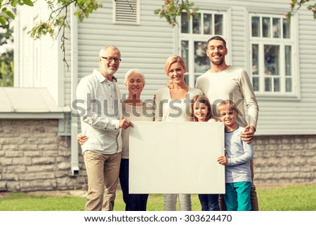 family, happiness, generation, home and people concept - happy family standing in front of house with white blank board outdoors