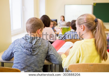 education, elementary school, learning and people concept - group of school kids with notebook writing test and helping in classroom