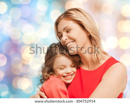people, motherhood, family and adoption concept - happy mother and daughter hugging over blue holidays lights background