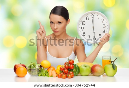 people, eating and diet concept - woman with healthy food holding big clock, pointing finger up and warning over green lights background